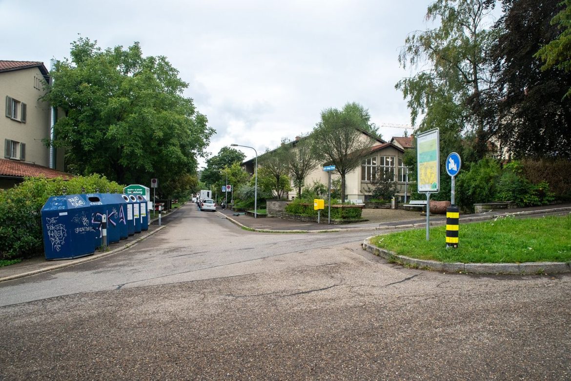 Colour-coded recycling bins line a residential street with clear labels on their lids.